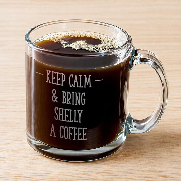 A glass mug filled with coffee, with the text "KEEP CALM & BRING SHELY A COFFEE" engraved on it.