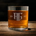 Front-facing product image of the engraved whiskey glass on a wooden table. The monogram and year layout are centered and easy to read.
