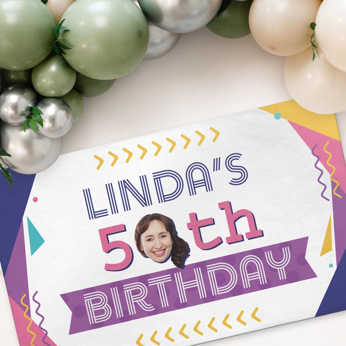 Personalized retro birthday banner displayed beneath a balloon garland, featuring a custom name, age, and face cutout.