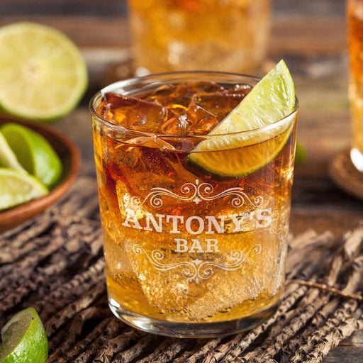 Personalized whiskey glass displayed with whiskey, ice, and fresh lime on a rustic wooden surface. The “Antony’s Bar” engraving stands out clearly, showing how the finished custom rocks glass looks in a stylish home bar setting.
