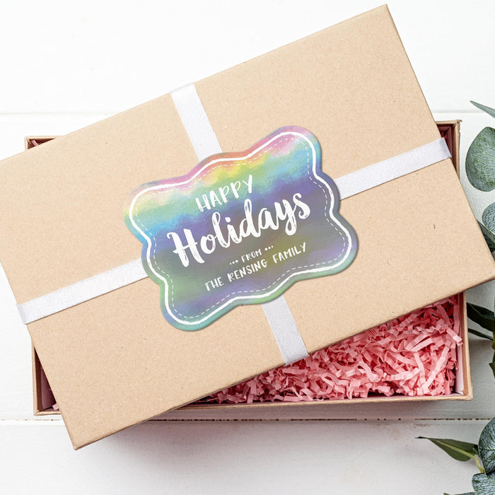 Personalized rounded rectangle Happy Holidays gift tag displayed on a kraft gift box with white ribbon and pink crinkle paper.