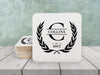 Laurel Monogram design shown on square paper coasters on a white wooden table.