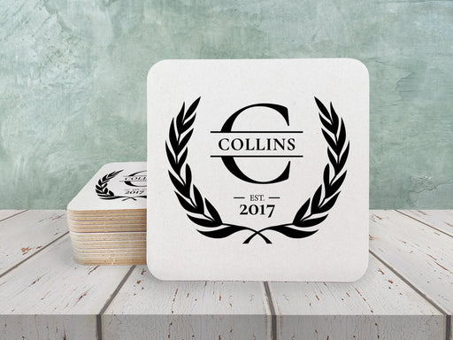 Laurel Monogram design shown on square paper coasters on a white wooden table.