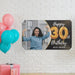 Personalized birthday banner displayed on a white brick wall with colorful balloons and party decorations.