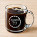 A glass mug filled with a dark liquid, likely coffee, with foam on top. The mug has an engraved design on it that says "BADASS MOM" and "LOVE. VIOLET".