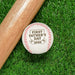 Baseball sits on grass next to baseball bat. Baseball has First Father's Day design engraved on it.