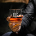 Close-up lifestyle photo of a personalized whiskey glass held in hand, showing the monogram and year engraving. The glass is filled with whiskey and ice, perfect for gifting.