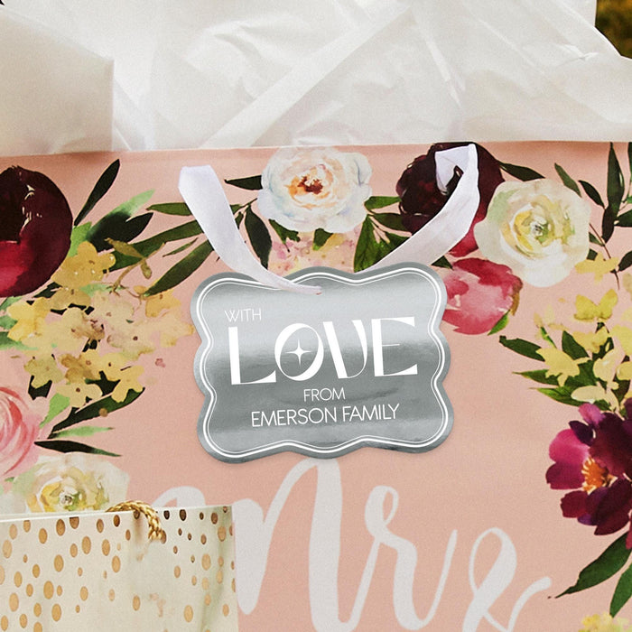 Floral wedding-themed flat lay featuring a personalized “With Love” wedding gift tag in metallic silver foil. Styled with romantic flowers and soft wedding décor accents.