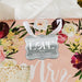 Floral wedding-themed flat lay featuring a personalized “With Love” wedding gift tag in metallic silver foil. Styled with romantic flowers and soft wedding décor accents.