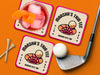 Custom square pulpboard coasters are shown sitting on a blue surface. Golf tees, a golf ball, and a golf club sit beside them. The coaster features design with illustrated golf ball and hole, custom name, age, year, and location, and vivid orange, cream, and pink color palette.