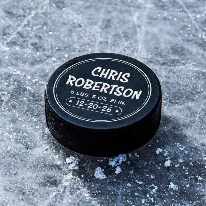 Personalized black hockey puck with a white UV printed birth announcement design featuring the baby’s name, weight, length, and birth date in a round layout.