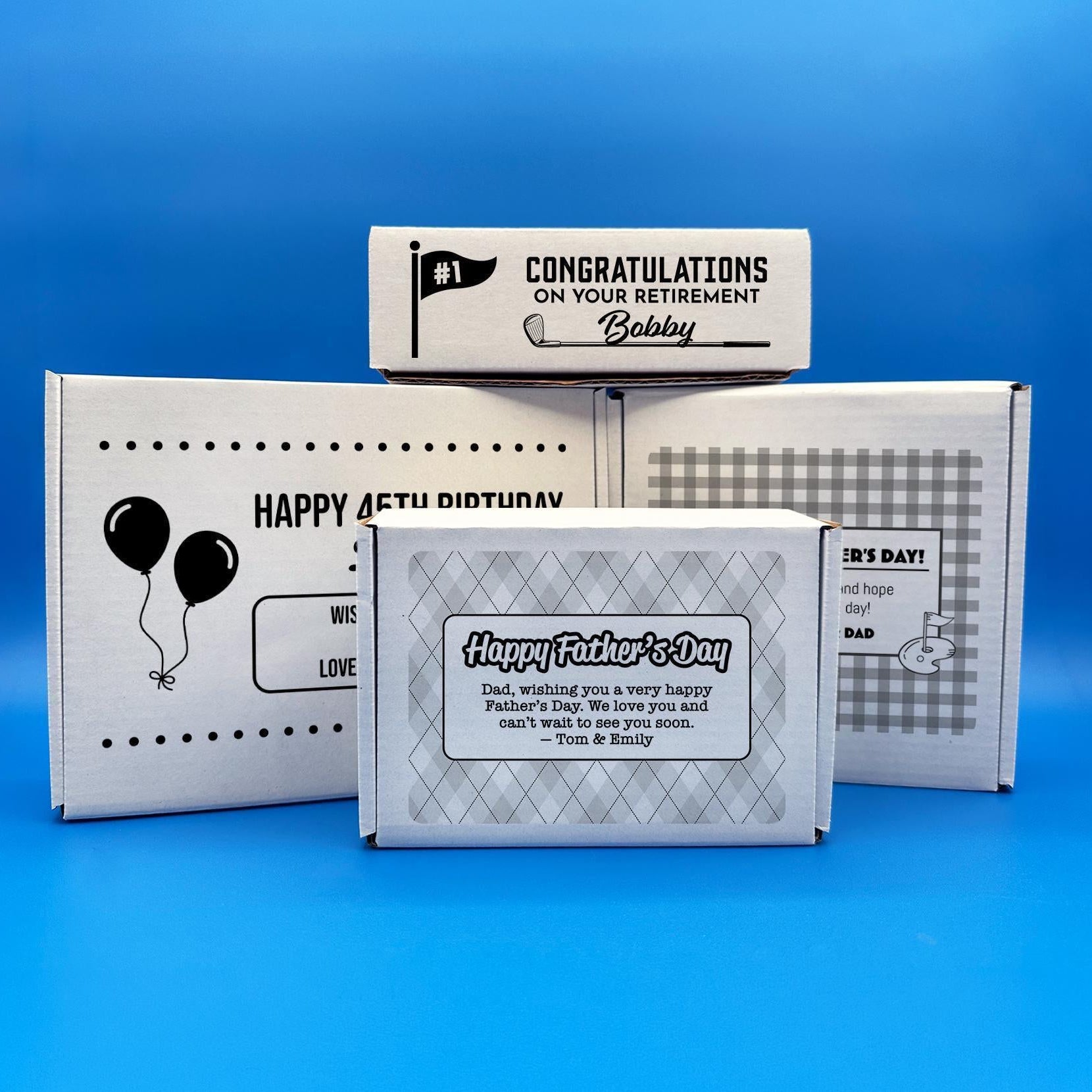 White custom cardboard gift boxes for golf balls with various designs and messages, including a "Happy Father's Day" box. The boxes are shown on a blue background.