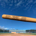 A custom engraved mini wooden baseball bat with text, held against a blue sky background.