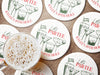 Custom round pulpboard coasters are shown sitting on a wooden surface with a beer mug on top of one. The custom coasters feature design printed with green sketched cocktails with golf balls and flags within the drinks, and red and green text.