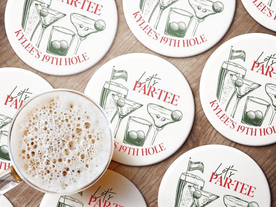 Custom round pulpboard coasters are shown sitting on a wooden surface with a beer mug on top of one. The custom coasters feature design printed with green sketched cocktails with golf balls and flags within the drinks, and red and green text.