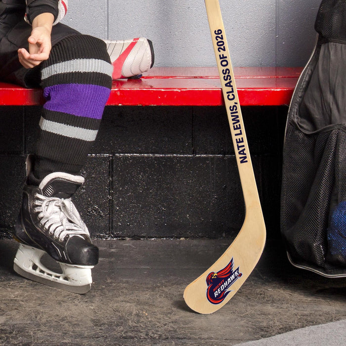 Lifestyle image of a hockey player in skates holding a personalized mini hockey stick with a team logo printed on the blade.