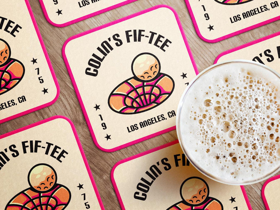 Custom square pulpboard coasters are shown laid out on a wooden surface. A beer mug is shown on top of a few of the coasters. The coaster features design with illustrated golf ball and hole, custom name, age, year, and location, and vivid orange, cream, and pink color palette.
