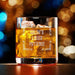 Elegant product photo of the engraved whiskey glass filled with whiskey and ice against a soft bokeh background. The custom design is centered and clearly visible, perfect for showcasing the finished personalized gift.