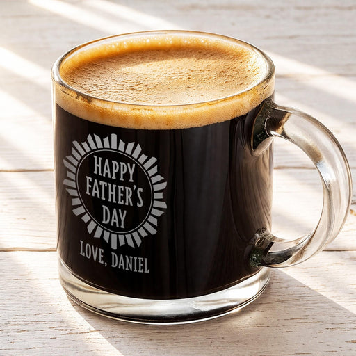 A glass mug filled with a dark liquid, likely coffee, with a foamy top. The mug has an engraved message that reads "Happy Father's Day Love, Daniel".