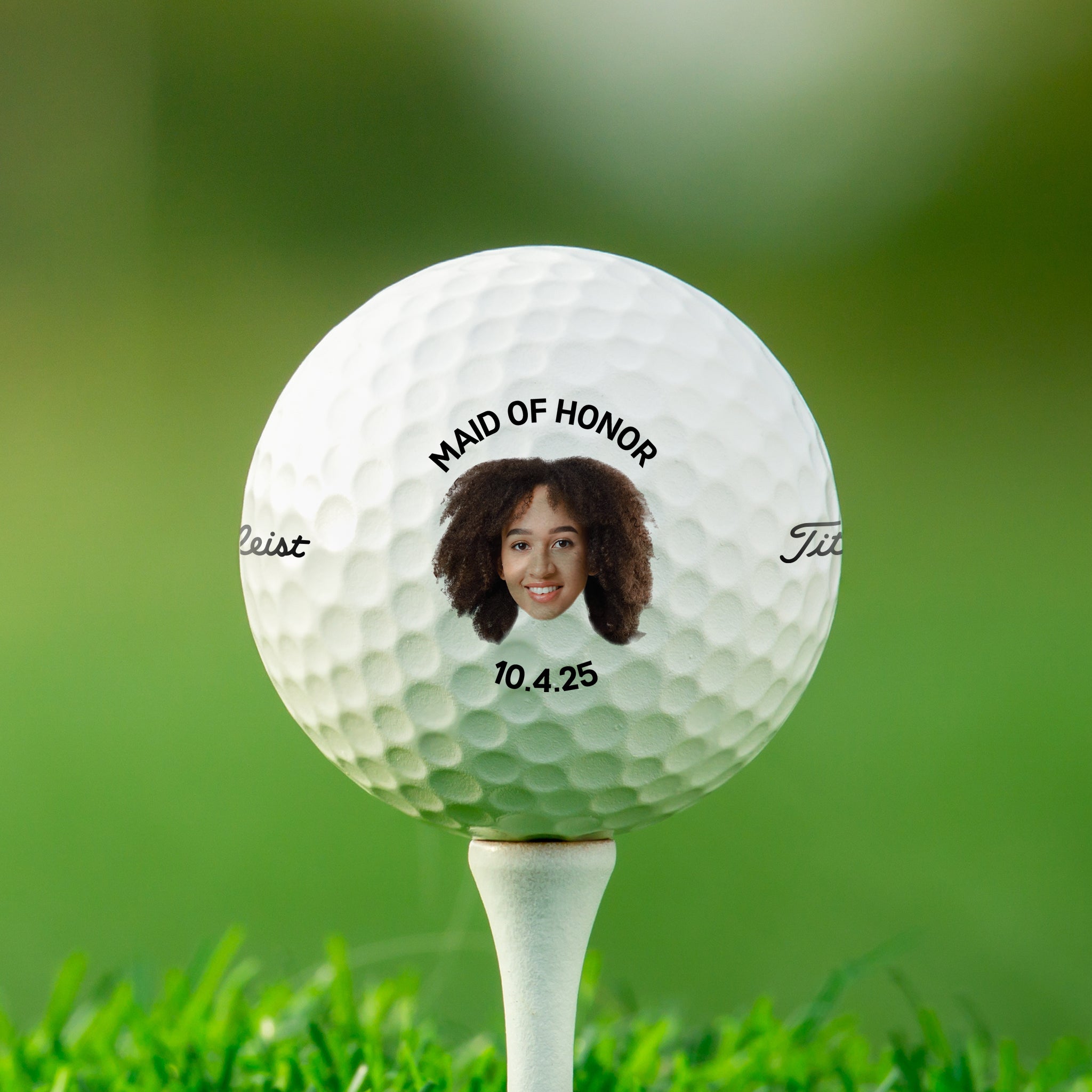 A golf ball with a picture of a smiling woman on it, placed on a grassy surface.