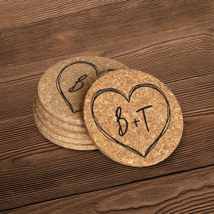 Round cork coasters featuring a large hand-drawn heart outline with personalized initials on a wood table.