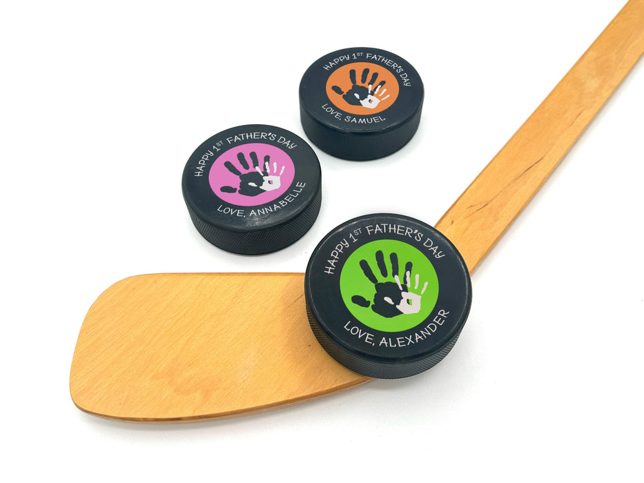 three hockey pucks with 1st fathers day designs printed on them with the colors green, pink, & orange with the names Alexander, Annabelle, and Samuel