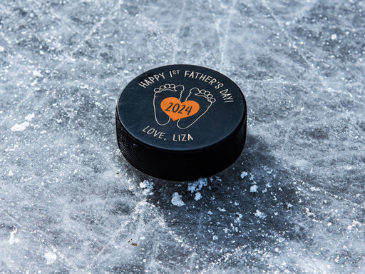 hockey puck ontop of ice with orange 1st Fathers Day footprint design with the name Liza printed on it