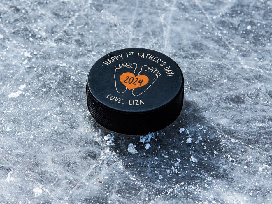 hockey puck ontop of ice with orange 1st Fathers Day footprint design with the name Liza printed on it
