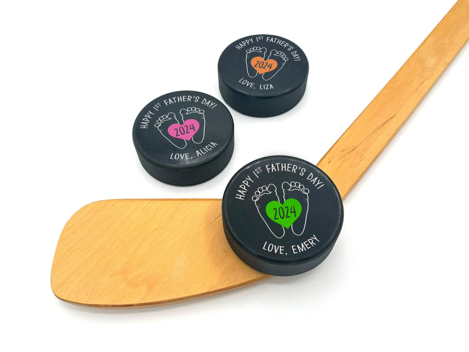 three hockey pucks with 1st fathers day designs printed on them with the colors green, pink, & orange with the names Emery, Alicia, and Liza