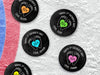 Multiple hockey pucks on top of ice rink with 1st fathers day footprint designs with different names and colors