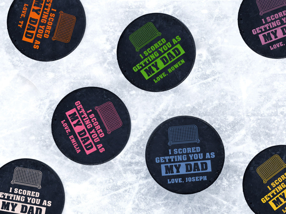 Multiple hockey pucks ontop of ice rink with I scored you as my dad designs printed ontop with different names and colors