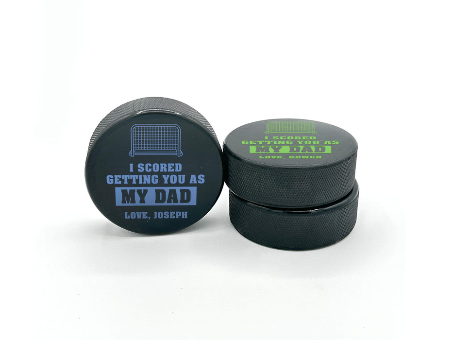 three stacked hockey pucks with printed  I scored you as my dad  designs in the color blue and green with the names Joseph and Rowen