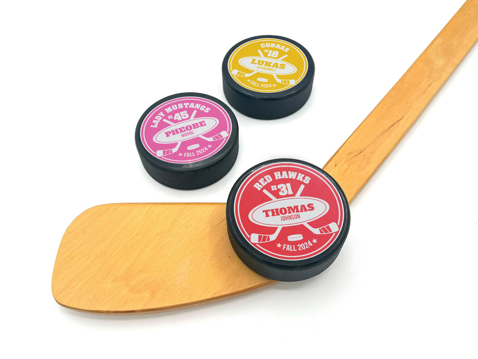 three hockey puck with a red, pink, and yellow player and team name design with a hockey stick design with the player and team name and information