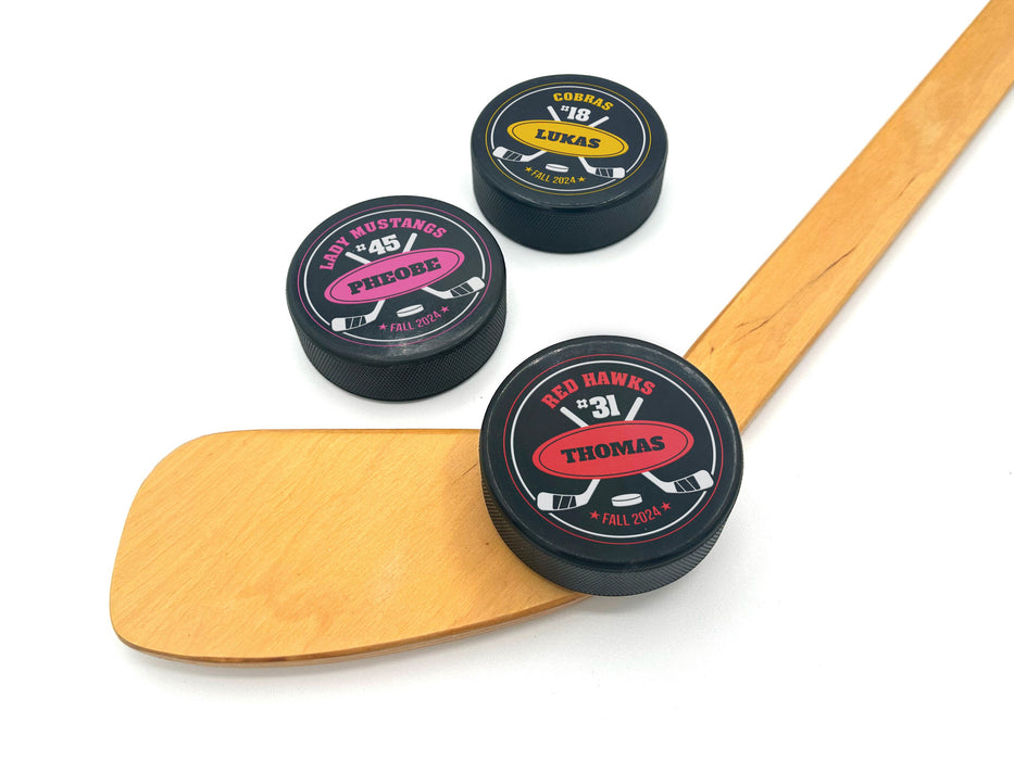 three hockey pucks with wooden hockey stick with red, pink, and yellow hockey team designs on white background