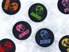 Multiple hockey pucks ontop of ice rink with player name & number with helmet designs with different names and colors