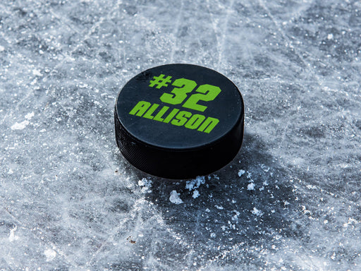 single hockey puck on ice rink with name and number design printed in green that says Allison number 32