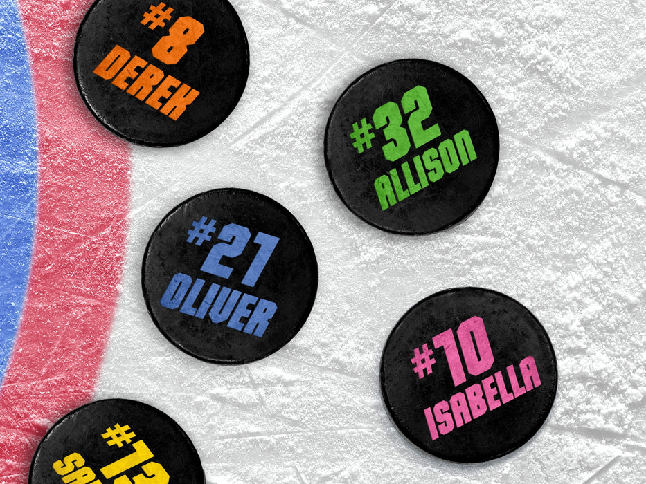Multiple hockey pucks ontop of ice rink with player name & number designs with different names and colors