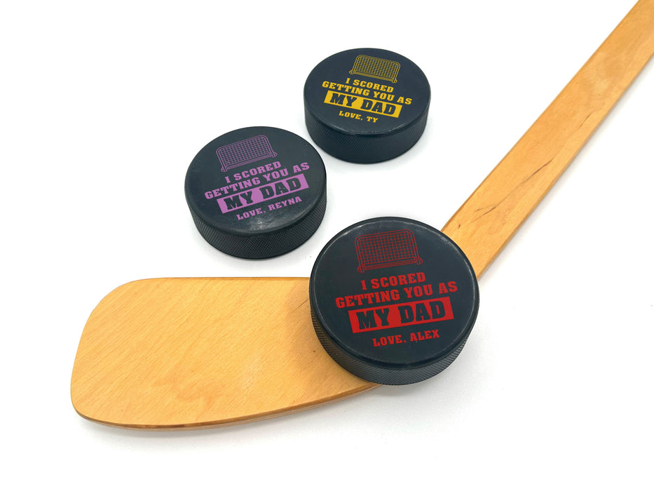 three hockey pucks with I scored you as my dad designs printed on them with the colors red, purple, & yellow with the names Alex, Reyna, and Ty