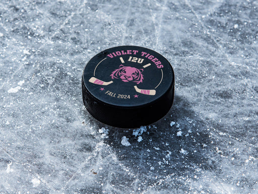 Hockey puck on ice rink with a purple tiger animal mascot design with the words Violet Tigers, 12U, Fall 2024