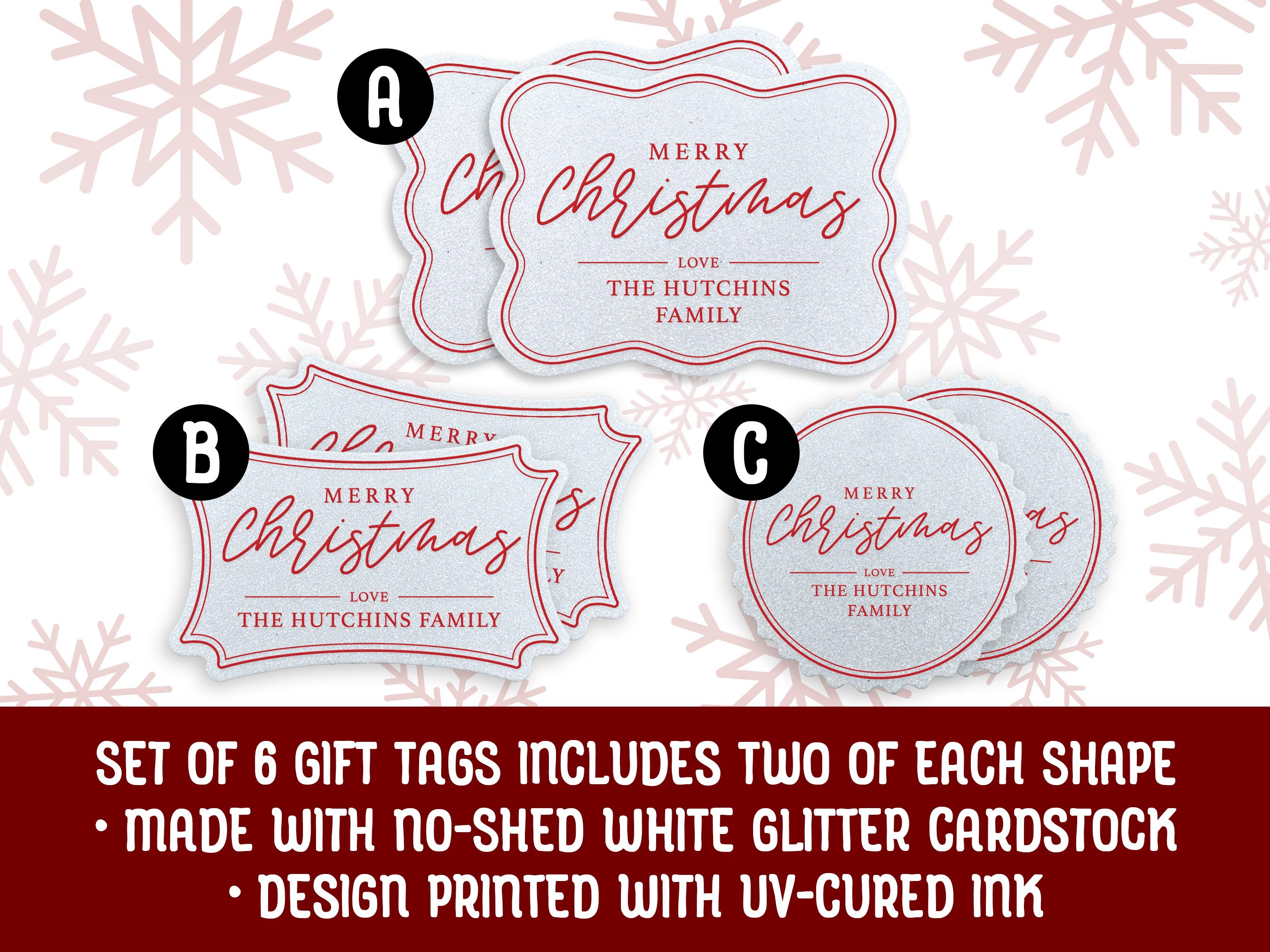 Text reads, Set of 6. Three white glitter cardstock Merry Christmas gift tags are shown on a white wooden surface. Pine tree branches and holly berries are shown above the tags.