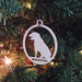 Ornament is shown hanging on Christmas tree with lights. Ornament design has a dog silhouette with the year and pet's name engraved on wooden ornament.
