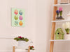 8x10 canvas with colorful easter artwork of rows of eggs and a baby chick on a white room wall surrounded by easter decor such as potted plants, birdhouses, and a wooden bunny statue