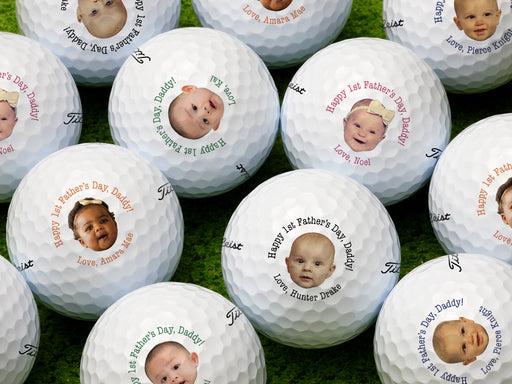 Multiple white titleist golf balls with first Father's Day baby photo design in all available color options on golf course grass