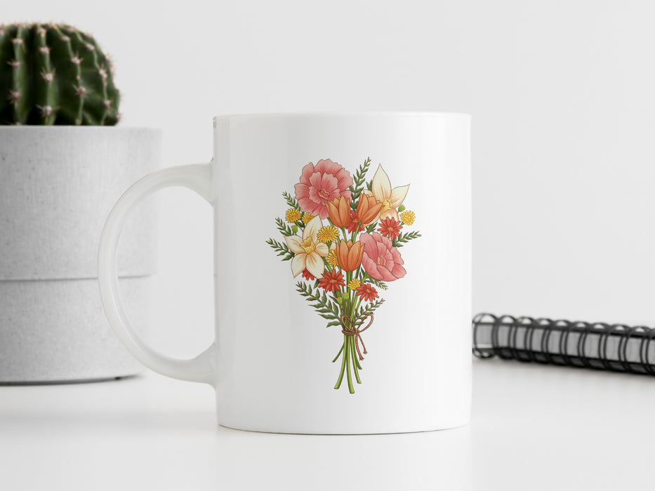 15 ounce ceramic mug featuring artwork of a bouquet of pastel spring flowers on a white table next to an spiral note book and a potted cactus