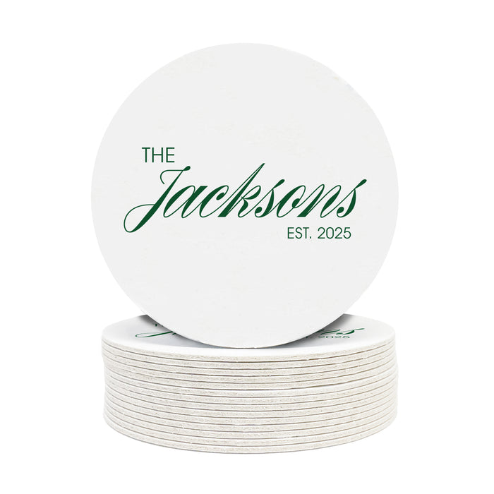 A stack of coasters are shown on a white background. Coasters feature Formal Last Name and Established Date design. This design has a white background and the happy couples last name and wedding year in emerald green writing.