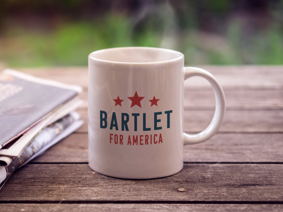 white mug on outdoor wooden table next to newspaper with red white and blue American design with red stars with typography that says Bartlet for America