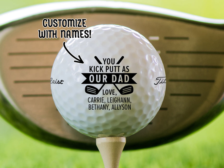Single white titleist golf ball with Kick Putt Dad design on wooden golf tee with golf club and golf course grass in the background. The text "customize with names" is above the ball with an arrow pointing toward it.