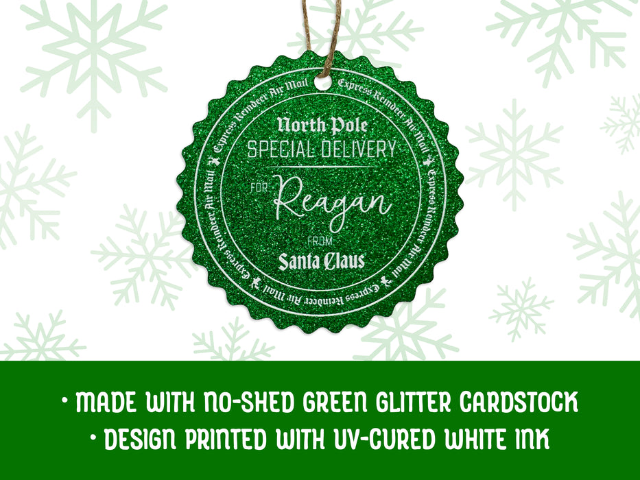 A green glitter hanging cardstock Santa gift tag is shown on a white background with green snowflakes. Text underneath the tag reads: Made with no-shed green glitter cardstock, Design printed with UV-cured white ink.