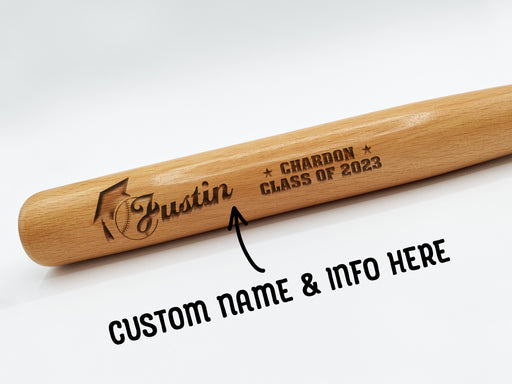 wooden mini baseball bat with custom laser engraved design that features a name with a graduate cap and says "Justin, Chardon, Class of 2023" on a white surface with and arrow and text that says "Custom Name & Info Here"