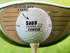 Single white Titleist golf ball with Shhh I'm Hiding From design on wooden golf tee with golf club and golf course grass in the background. The text "customize with a name" is above the ball with an arrow pointing toward it.